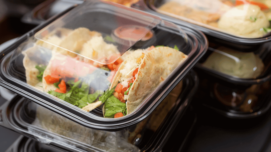 To-go case with clear top and black base with three tacos and sauce inside, stacked on other to-go cases