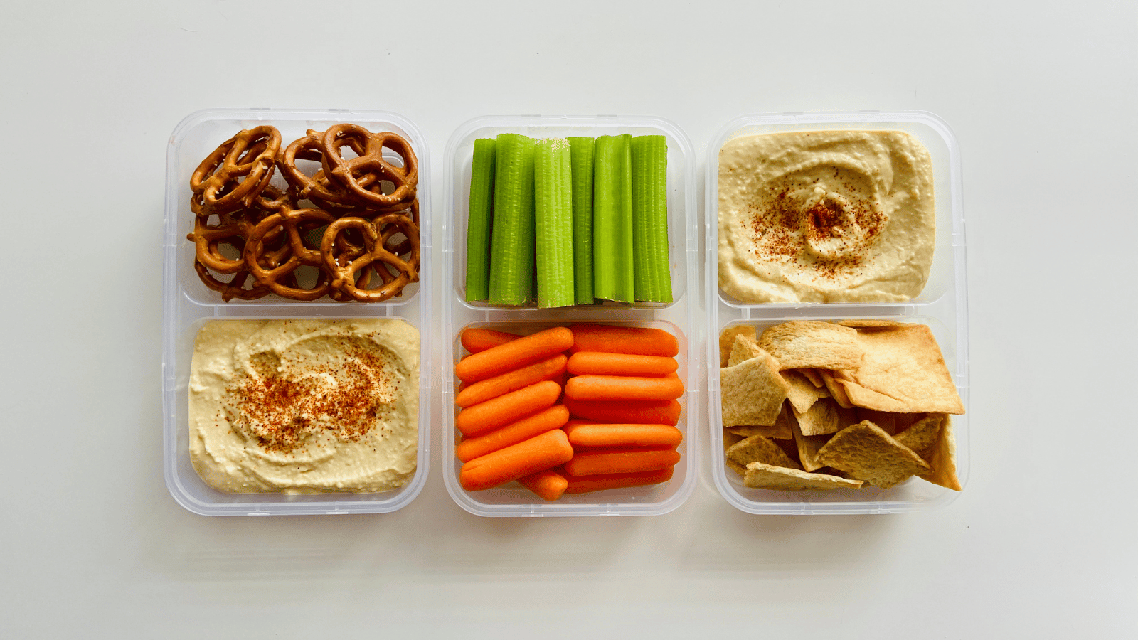 Six containers. One each with pretzels, carrots, celery and pita chips. Two each with hummus.